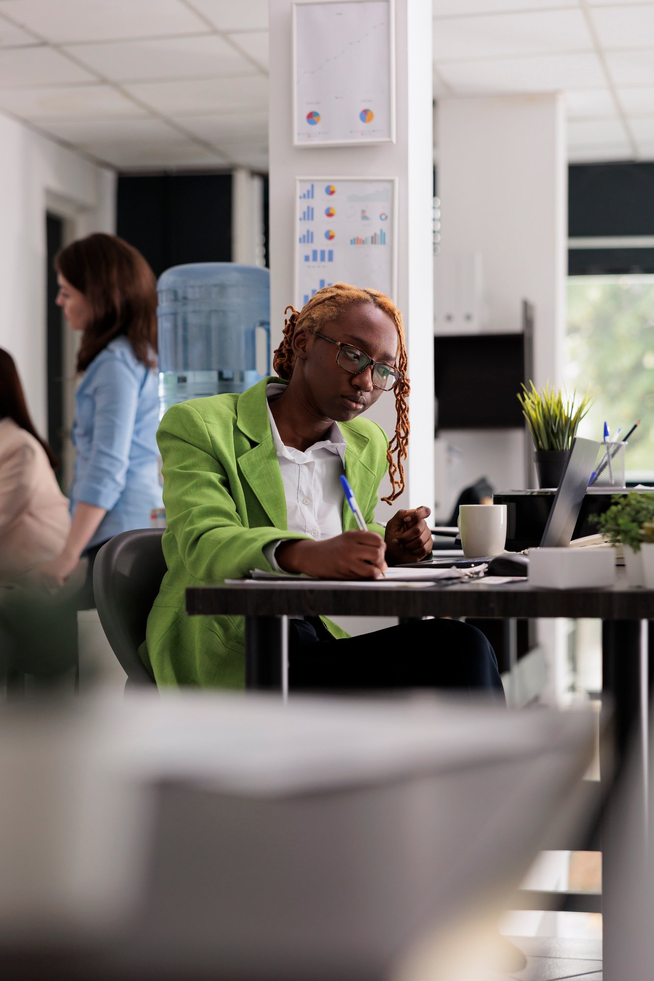 employee-coworking-open-space-writing-clipboard-looking-laptop-sitting-workplace-desk-young-african-american-woman-working-with-company-documents-taking-notes